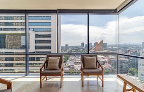 Un appartement situé dans un immeuble de grande hauteur, doté d’un grand balcon, de deux chaises en bois et offrant une vue sur le paysage urbain.