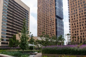 Un quartier urbain moderne, avec de hauts immeubles, un jardin aménagé aux fleurs violettes et un ciel dégagé.