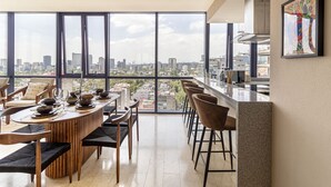 A modern dining area with a panoramic city view, a kitchen with bar stools, and a large window. - Miyana by Kukun (Mexico City)