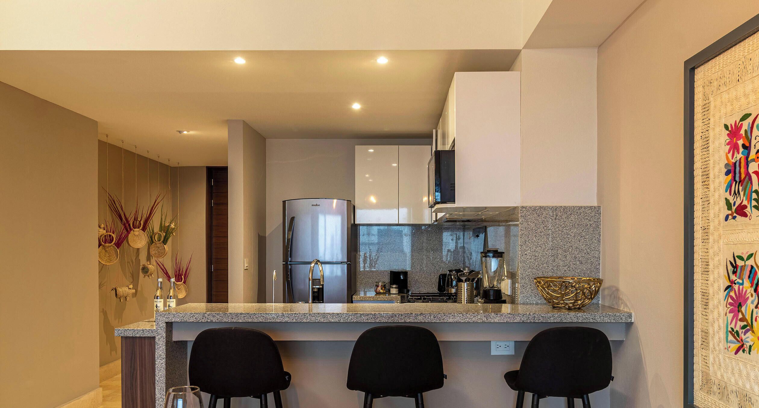 Uma cozinha moderna com bancada de granito, eletrodomésticos de aço inoxidável e banquetas pretas.