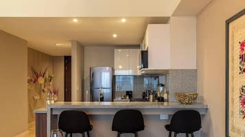 Uma cozinha moderna com bancada de granito, eletrodomésticos de aço inoxidável e banquetas pretas.