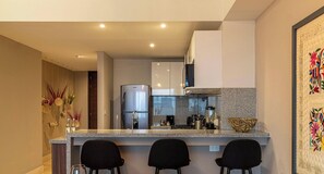 Une cuisine moderne dotée d’un comptoir en granit, d’appareils électroménagers en acier inoxydable et de tabourets de bar noirs.
