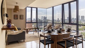 A modern living room with a large city view, a dining area with a round table, and a cozy seating area. - Miyana by Kukun (Mexico City)