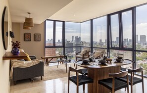 Ein modernes Wohnzimmer mit weitreichendem Stadtblick, einem Essbereich mit rundem Tisch und einer gemütlichen Sitzecke.