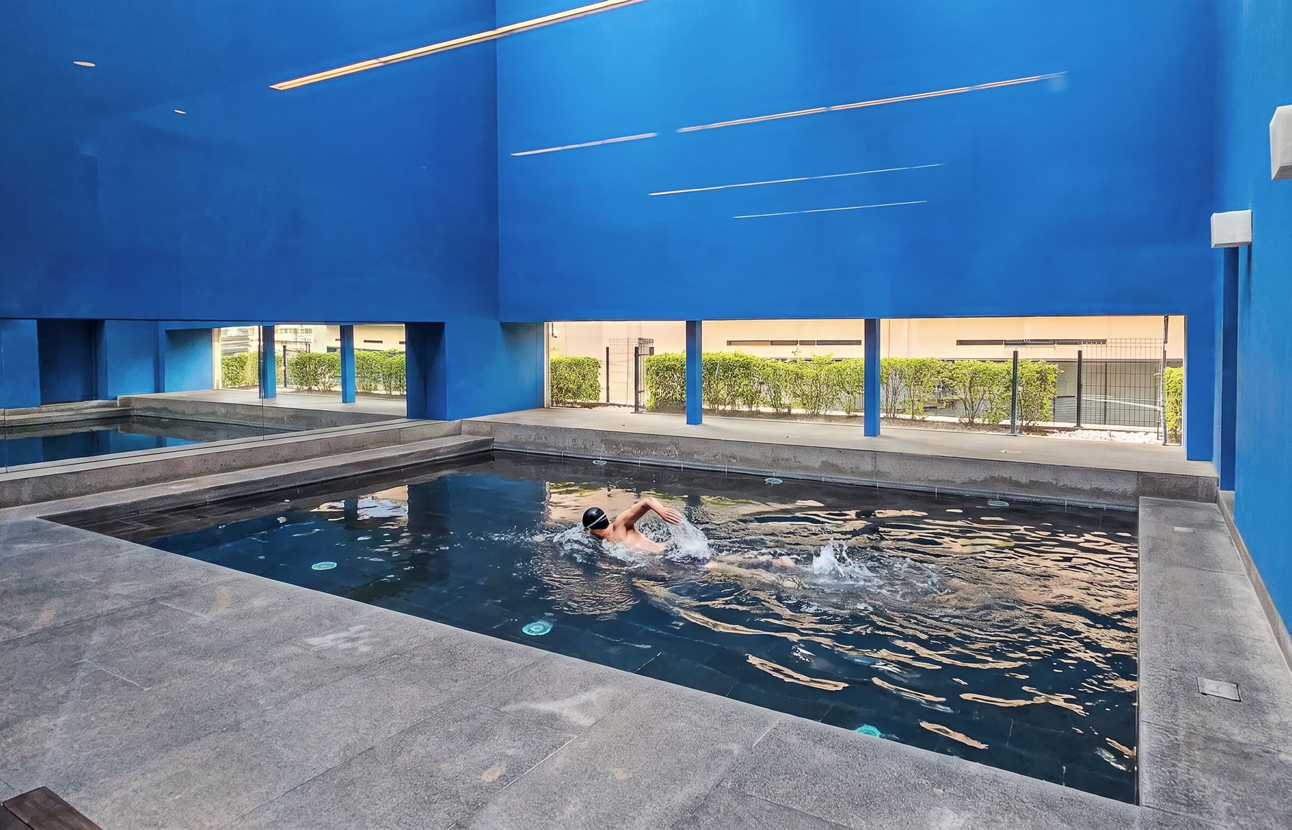 Una piscina con una persona nadando, rodeada de paredes azules y una vista despejada del exterior.