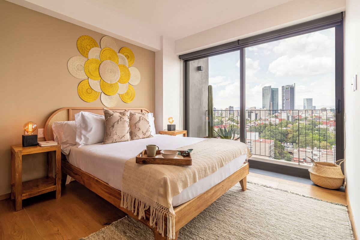 Une chambre avec vue sur la ville, un lit en bois, une table de chevet avec une lampe et une œuvre d’art murale.