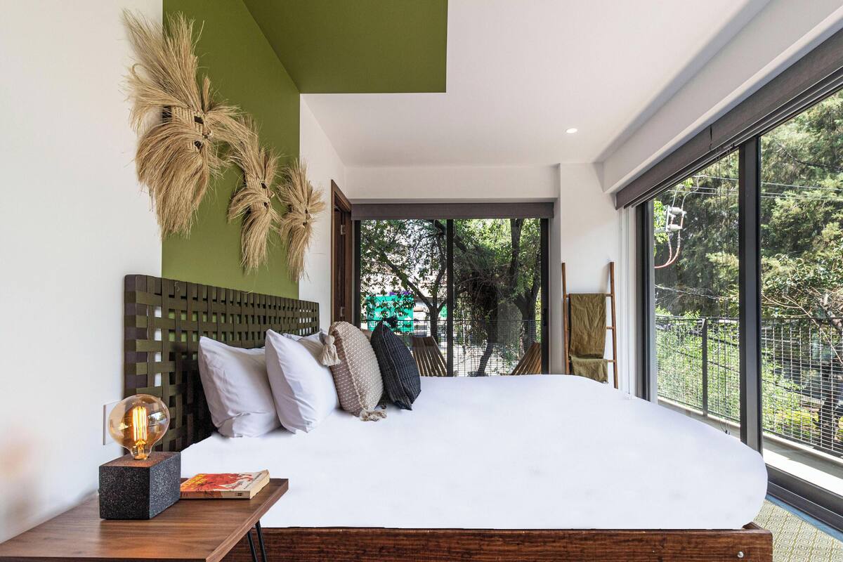 Une chambre moderne avec un grand lit, une tête de lit en bois et une vue sur la verdure.