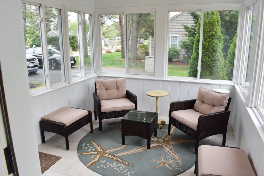 A sunroom with wicker furniture, a glass coffee table, and a starfish-patterned rug.