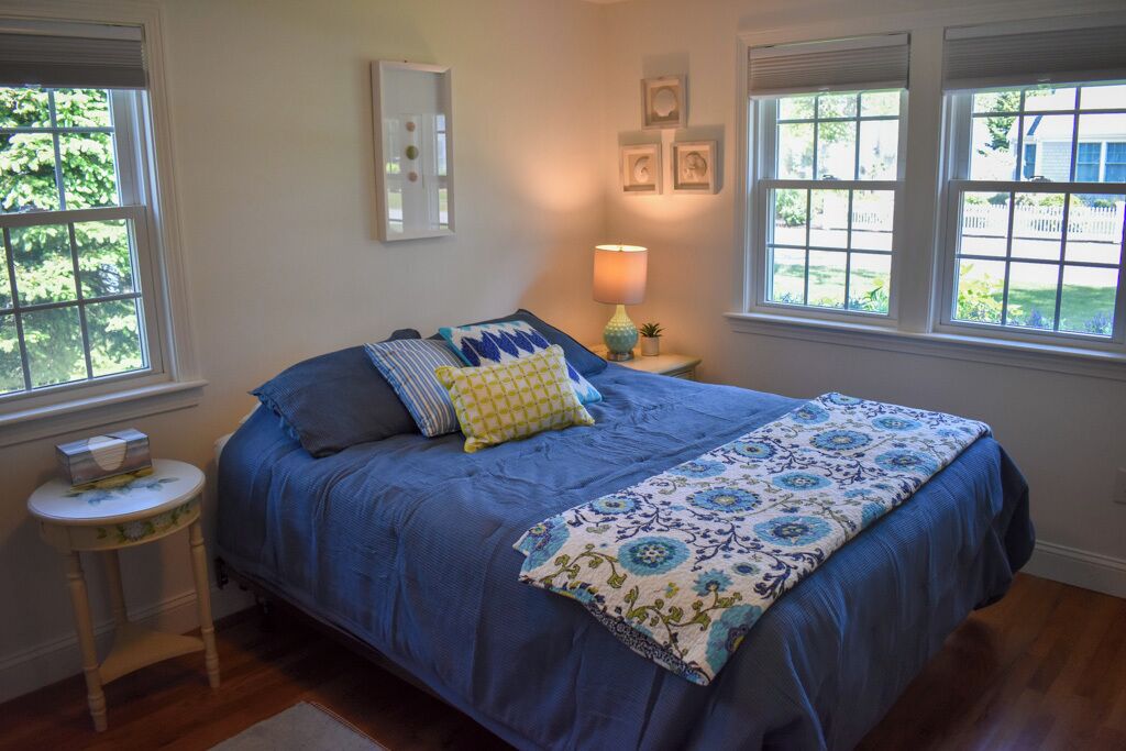 A bedroom with a large bed, two bedside tables, a lamp, and a window with a view of a fence and trees.
