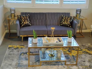 A living room with a gray sofa, two patterned pillows, a glass coffee table with decorative items, and two side tables with lamps. - Sports fans & Foodies King with Balcony, Queen, pool minutes to Golf & Airport  (Phoenix)