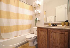 A bathroom with a striped shower curtain, a toilet, a sink with toiletries, and a mirror above the sink. - Sports fans & Foodies King with Balcony, Queen, pool minutes to Golf & Airport  (Phoenix)