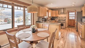 A modern kitchen with wooden cabinets, a central island, and large windows offering a view of the outdoors. - Stunning Gallatin Gateway Mountain Retreat! (Gallatin Gateway)