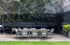 An outdoor patio with a table and chairs, surrounded by a black wall and greenery. - Magenta by Kukun (Mexico City)