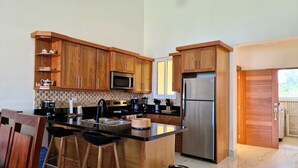 Eine moderne Küche mit Holzausbau, Edelstahlgeräten, einer Marmorarbeitsplatte und einer kleinen Bar mit Hockern.