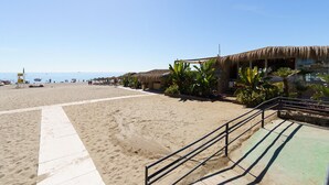 Une plage avec un bâtiment à toit de chaume, une tour de surveillance pour les sauveteurs et un ciel dégagé.