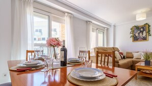 Un coin repas avec une table en bois dressée pour quatre personnes, un vase de fleurs et une bouteille de vin.