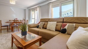 Un salon avec un canapé beige, une table basse en verre et un coin repas comprenant des chaises et une table en bois.