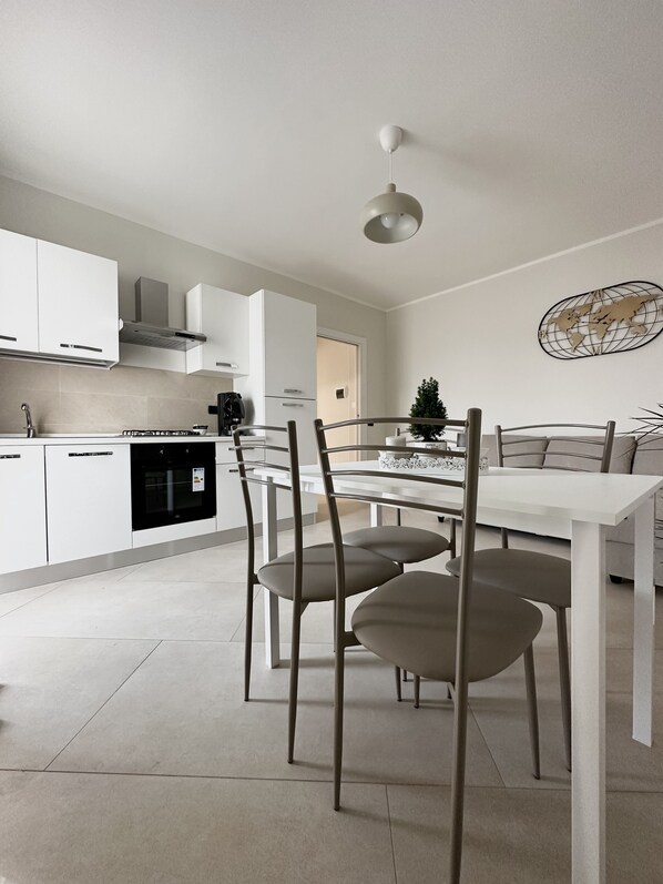 A modern kitchen with white cabinets, a black oven, and a dining area with a white table and chairs.