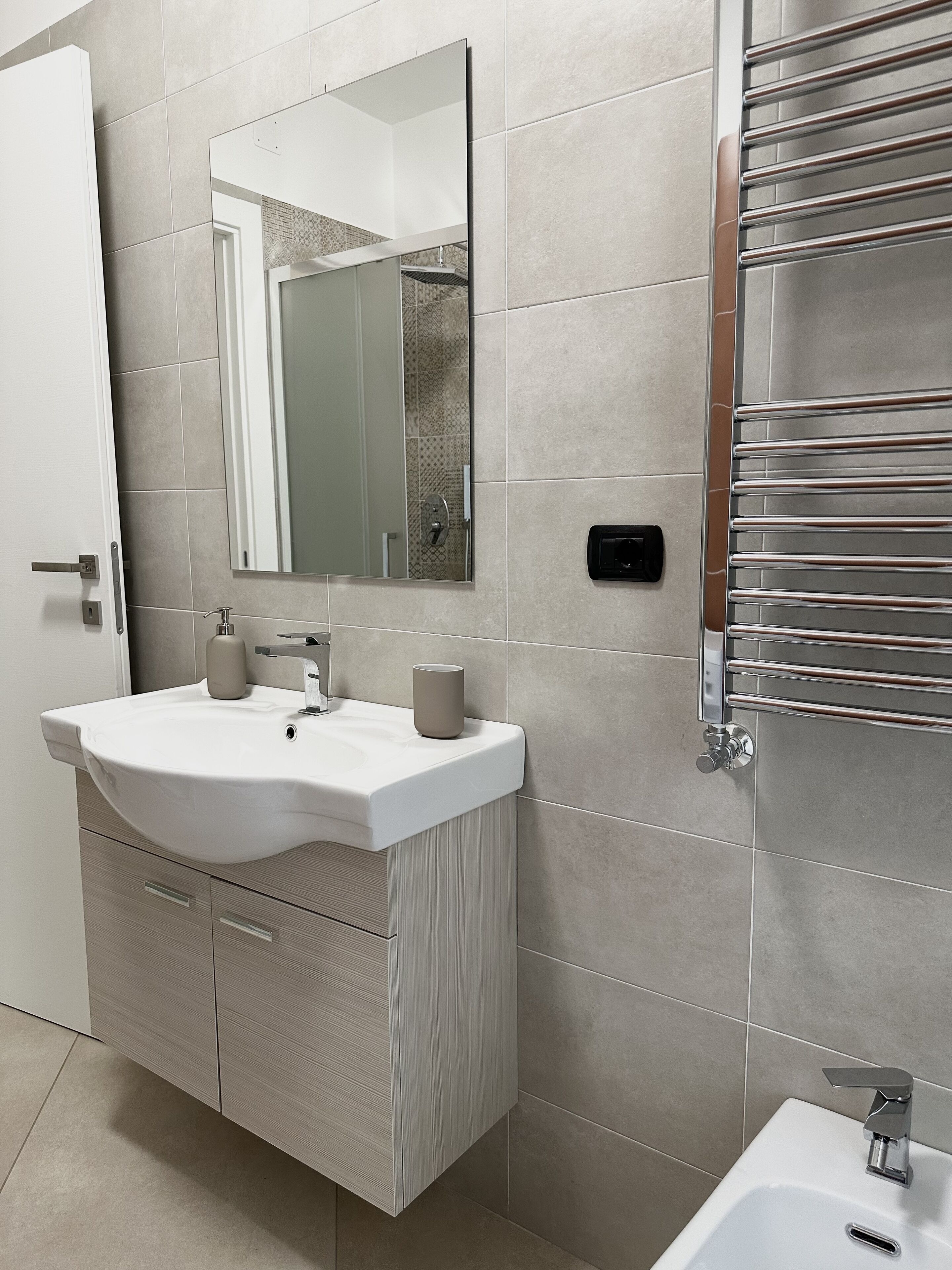 Un baño moderno con lavamanos blanco, espejo y toallero cromado.
