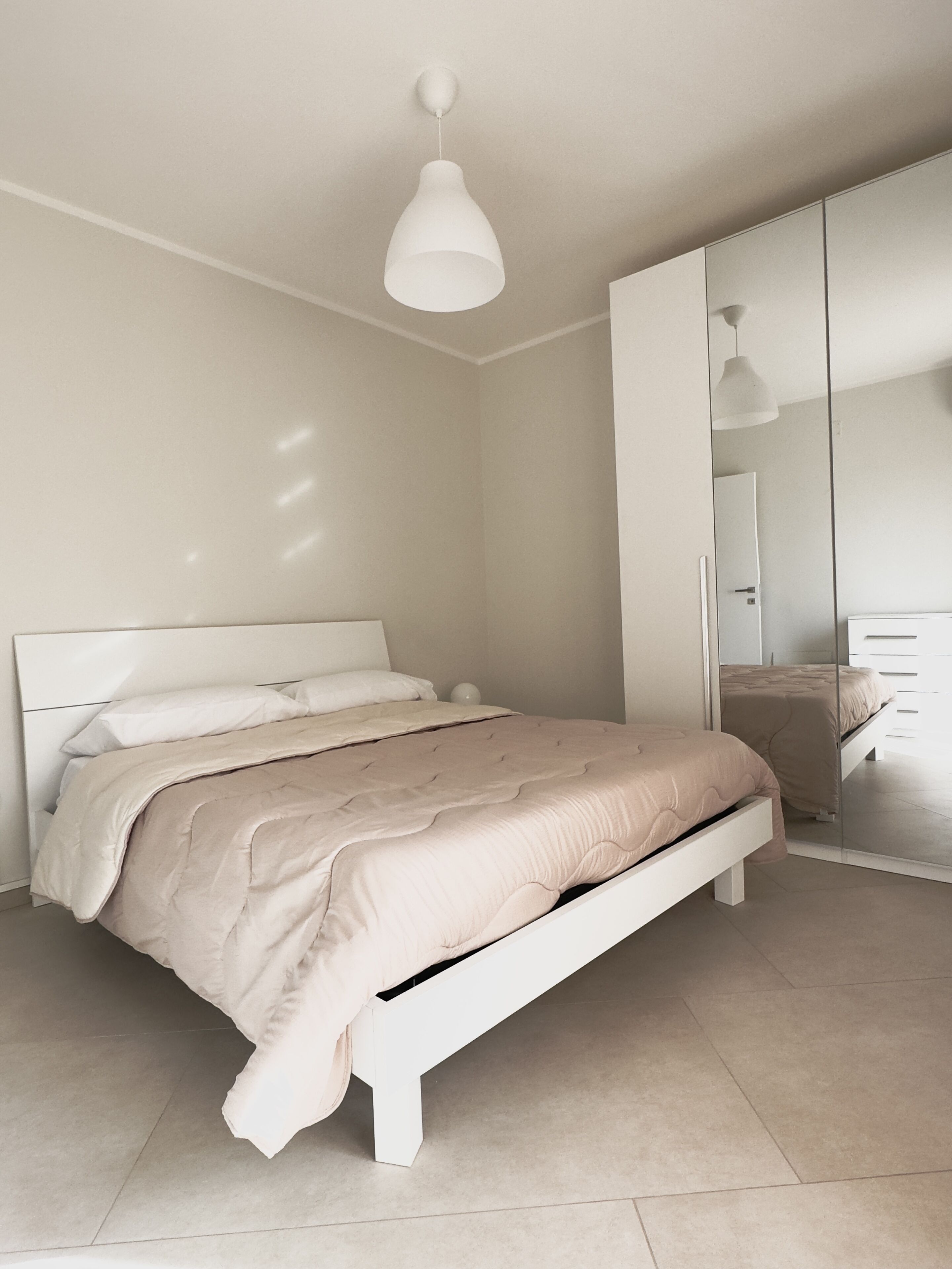 Ein modernes Schlafzimmer mit einem weißen Bett, einem großen Spiegel und einer Pendelleuchte.