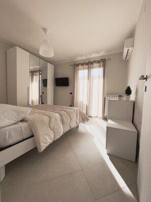 A modern bedroom with a bed, a wardrobe, a small desk, a television, and a radiator.