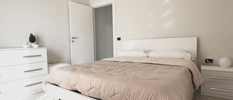 A modern bedroom with a bed, white dresser, and a pendant light.