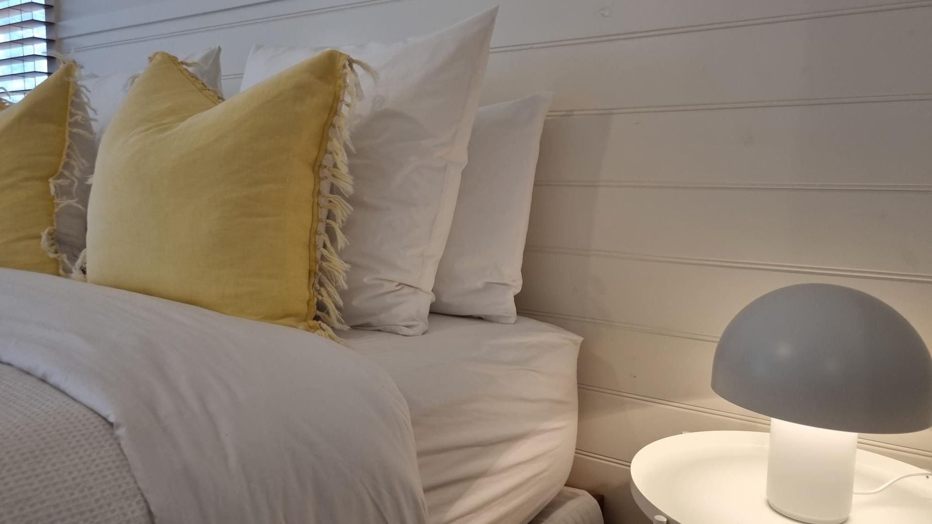 A bed with white and yellow pillows, a bedside table with a lamp, and a white wall.