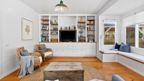 A living room with a TV, bookshelves, wicker chairs, and a window seat.