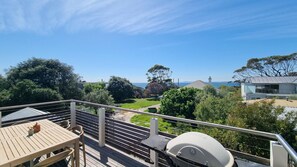 En balkon med et bord og stole, grill og havudsigt samt grønne omgivelser.