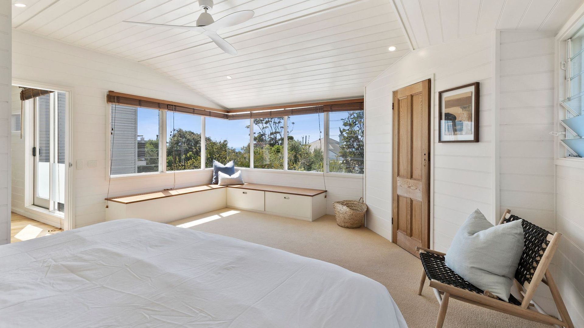 A bedroom with a large bed, built-in bench seating, a ceiling fan, and large windows offering a view.