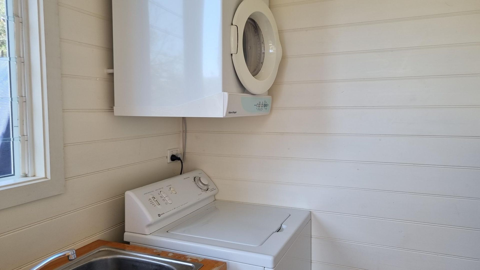 A laundry room with a washing machine and a dryer, a window, and a wall-mounted toilet.