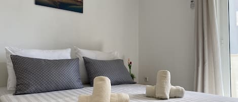 A neatly made bed with striped bedding, two pillows, and rolled towels.