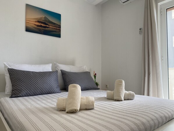 A neatly made bed with striped bedding, two pillows, and rolled towels.