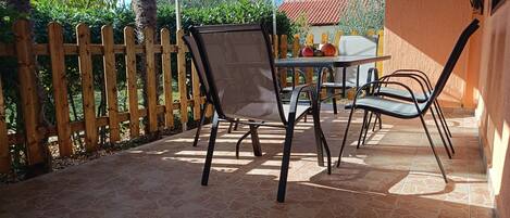An outdoor patio with a table and chairs, a wooden fence, and a tiled floor.