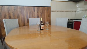 A round wooden table with two wine glasses and a bottle of wine, surrounded by chairs.