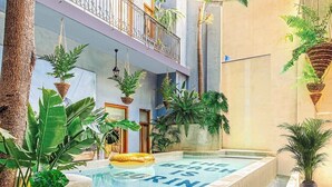 En inomhuspool med trappsteg som leder ner i den, omgiven av olika växter och en byggnad med balkonger.