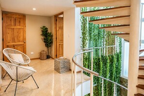 Un intérieur moderne avec une porte en bois, une chaise en osier, une plante en pot et un escalier doté d’une rampe en métal.