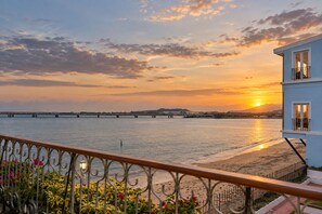 A coastal view with a sunset, a bridge in the distance, and a building with a balcony.