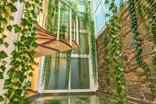 A spiral staircase with a glass railing, surrounded by lush green ivy, leading to a glass door.