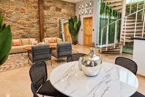 Un intérieur moderne avec un mur en pierre, un canapé, une table basse et un coin repas comprenant des chaises et une table en marbre.