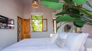 Un dormitorio con una cama grande, una puerta de madera, una ventana y un televisor montado en la pared.