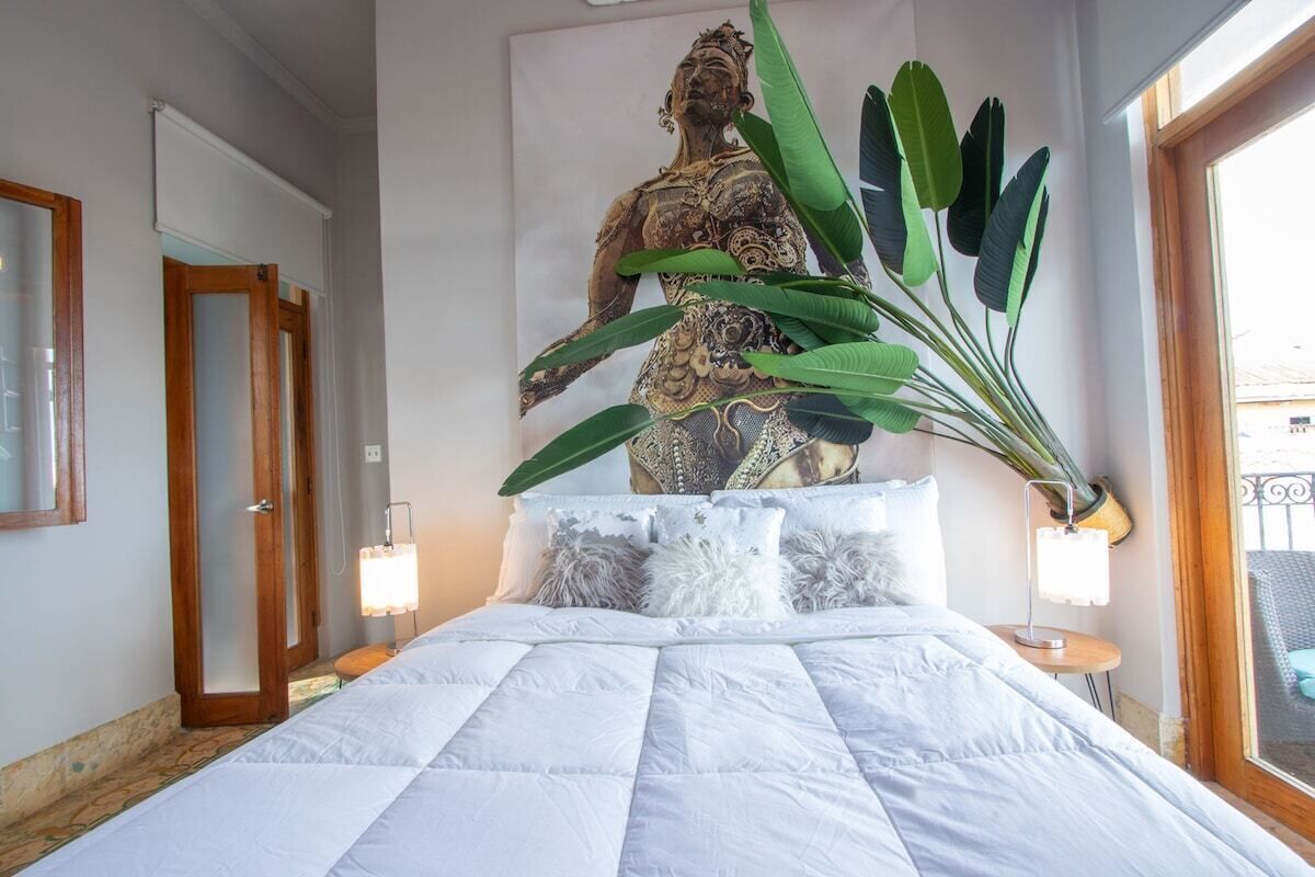 Ein Schlafzimmer mit einem Bett, einer großen Wandstatue, einer Topfpflanze und einem Fenster.