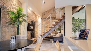 Ein modernes Interieur mit einer Steinwand, einer Treppe, einer Essecke mit Tisch und Stühlen sowie einem Laptop auf einem Schreibtisch.