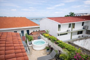Une terrasse sur le toit avec un jacuzzi, une vue sur la mer et un bâtiment dont le toit est recouvert de tuiles rouges.