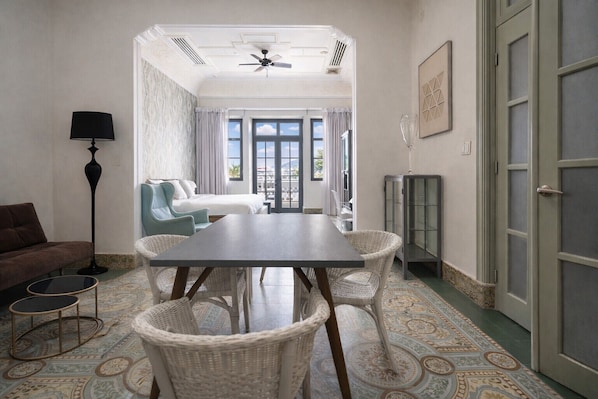 A room with a dining table, wicker chairs, a sofa, a floor lamp, and a view of the outside through large windows.