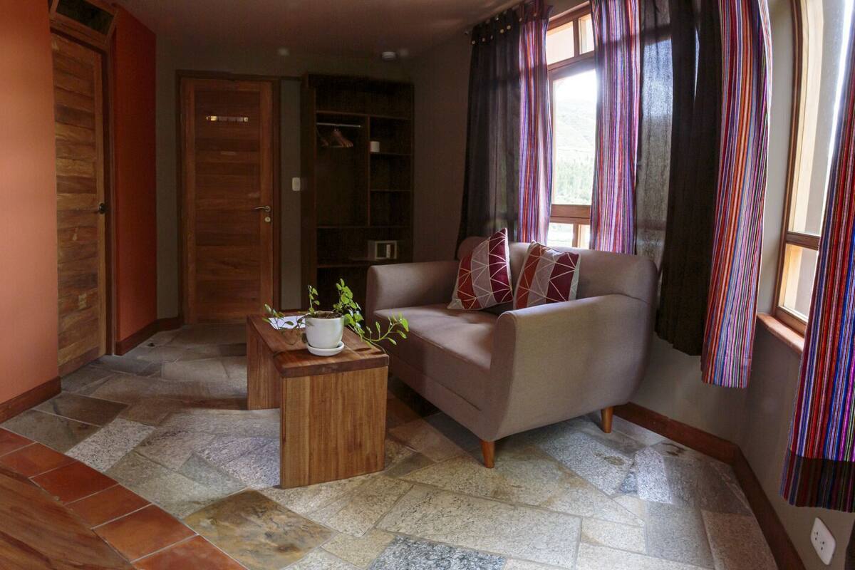 A hotel room with two beds, a wooden floor, a sofa, and a small table with a plant.