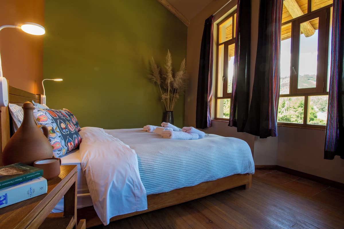 A neatly made bed with towels, a bedside lamp, and a vase with pampas grass.
