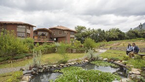 A two-story house with a patio and a pond. - Fleur Lodge (Acopampa)