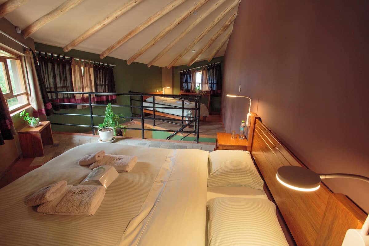 A bedroom with a large bed, a bedside table with a lamp, a window with curtains, and a balcony with a railing.