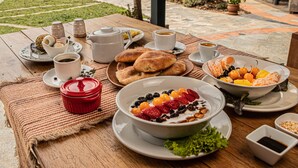 A wooden table set with breakfast items including bread, fruit, coffee, and a bowl of yogurt with berries. - Fleur Lodge (Acopampa)